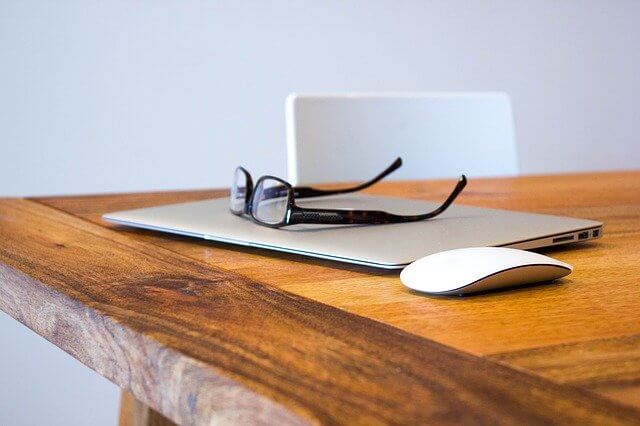 Laptop on desk with reading glasses laid on top