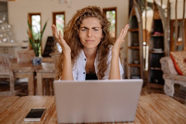 Frustrated woman sitting in front of laptop with her hand thrown up in the air