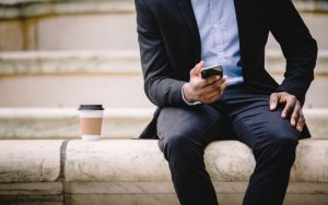 Man sitting outside with coffee, using smartphone to stay connected outside the office