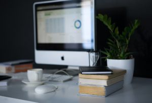 Computer showing blurred-out data, with a cup of coffee and stack of books in the foreground