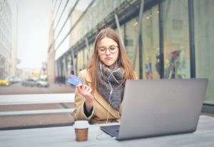Woman sitting at laptop and looking at a credit card as if considering website security