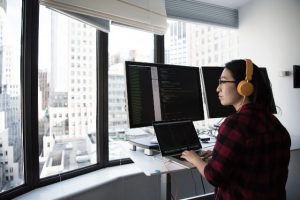 Woman working on computer with multiple monitors while looking out the window.