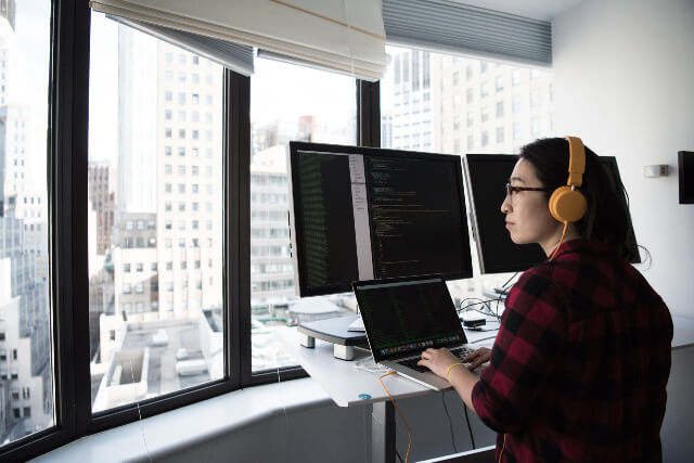 Woman working on computer with multiple monitors while looking out the window.