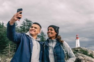 Man and woman taking selfie outdoors with a lighthouse in the background