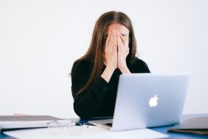 Woman in distress, sitting in front of open laptop with her face in her hands