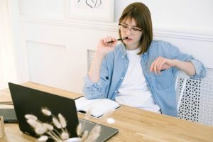 Woman chewing on pencil and staring at computer and blank journal