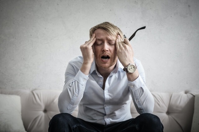 Man sitting on couch with glasses in his hand and fingers pressed to his temples