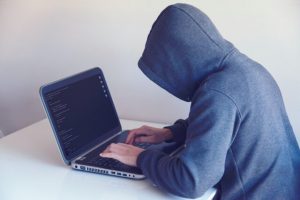 Man in dark hoodie hunched over laptop