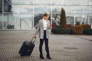 Woman standing at airport with suitcase, checking smartphone