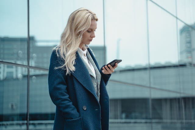 Woman standing outside looking confused while reading a text message
