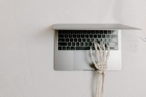 Skeleton arm typing on an open laptop.