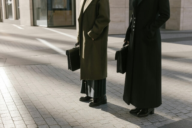 Man and woman in business coats, standing on the sidewalk, holding briefcases
