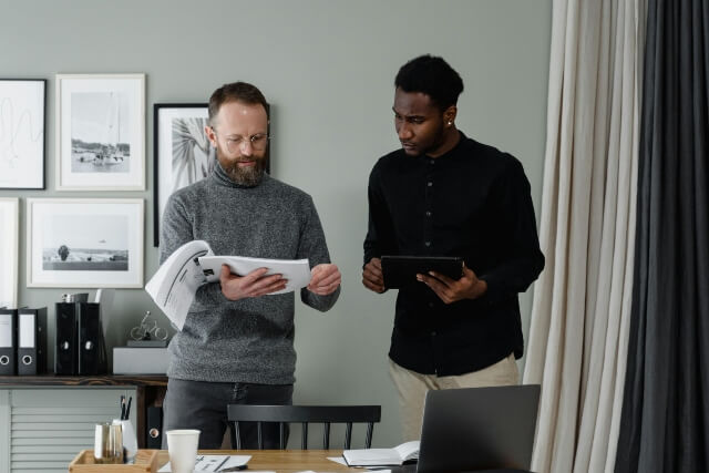Two men dressed in business casual reviewing a printed AI policy and a tablet computer.