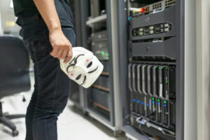 Man (view from waist down) standing in front of a server, holding an "anonymous" mask in his hand.