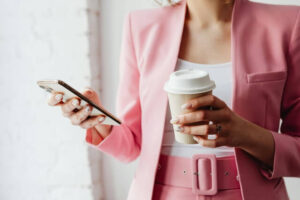 Closeup of woman in a pink suit holding a cup of coffee and a smartphone