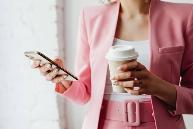 Closeup of woman in a pink suit holding a cup of coffee and a smartphone