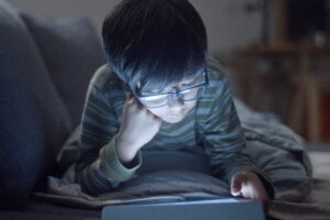 Young boy on a couch with his face illuminated by a table screen he is viewing