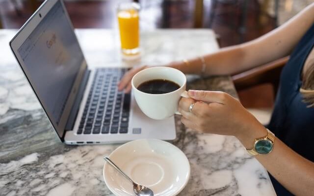 A woman's hands holding a coffee cup and typing on a laptop