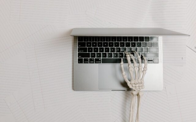 Skeleton arm typing on an open laptop.