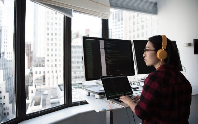 Woman working on computer with multiple monitors while looking out the window.