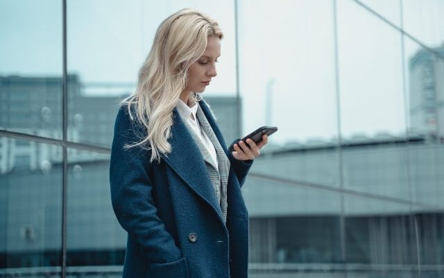 Woman standing outside looking confused while reading a text message