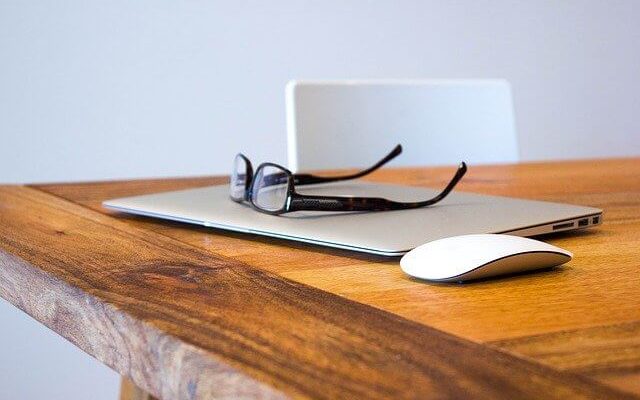 Laptop on desk with reading glasses laid on top