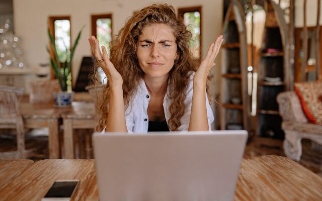 Frustrated woman sitting in front of laptop with her hand thrown up in the air