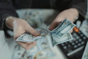 Woman's hand counting out hundred dollar bills. Blurred, in the background can be seen additional hundred dollar bills on a table and a calculator.