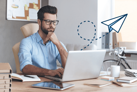 Man looking at laptop computer as a paper airplane flies off the screen and into the office