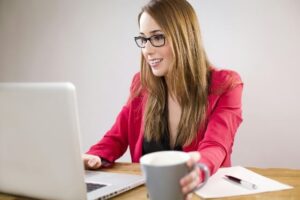 Smiling woman in bright pink business attire working on a laptop while drinking coffee