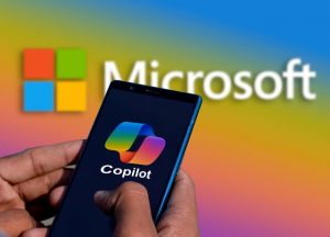 Hands holding a smartphone with the Microsoft Copilot logo. In the background is the Microsoft logo.
