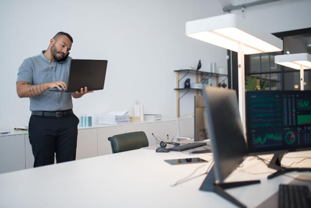 Man in business attire holding a laptop in one hand hand while talking on a cell phone
