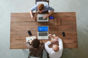 Three business professionals sitting at a table with open laptops having a discussion about cloud waste.