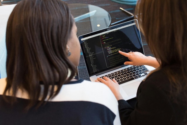 Two women sitting at a desk looking at a computer screen together