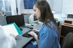 Nurse completing documentation on a laptop. She is looking at patient files being held by a doctor besider her. Her face shows concern.