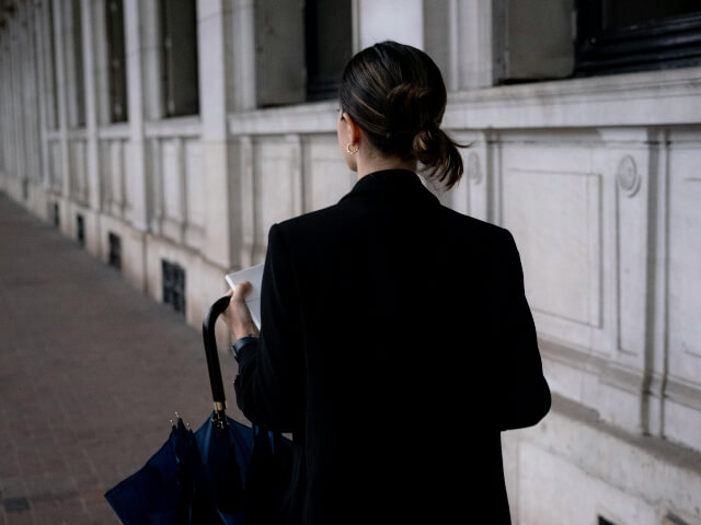 Woman walking away from her former place of employment carrying papers and an umbrella