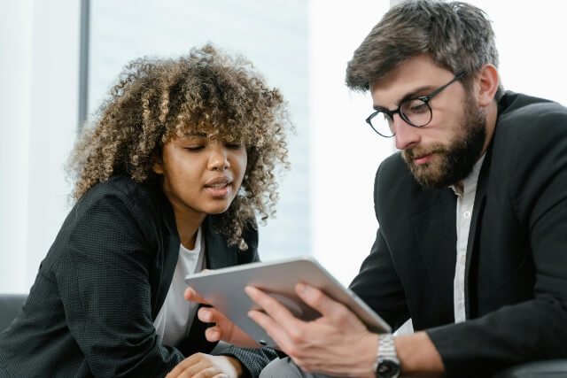 Man and woman in business attire, sitting and reading from a tablet together