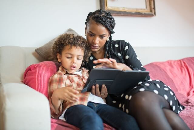 A mother and her son sitting on the couch, reviewing parental controls on a tablet device